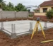 Coimbatore house plot with a newly laid foundation, a surveyor's tripod and measuring tape on the ground, and the boundary wall partly built